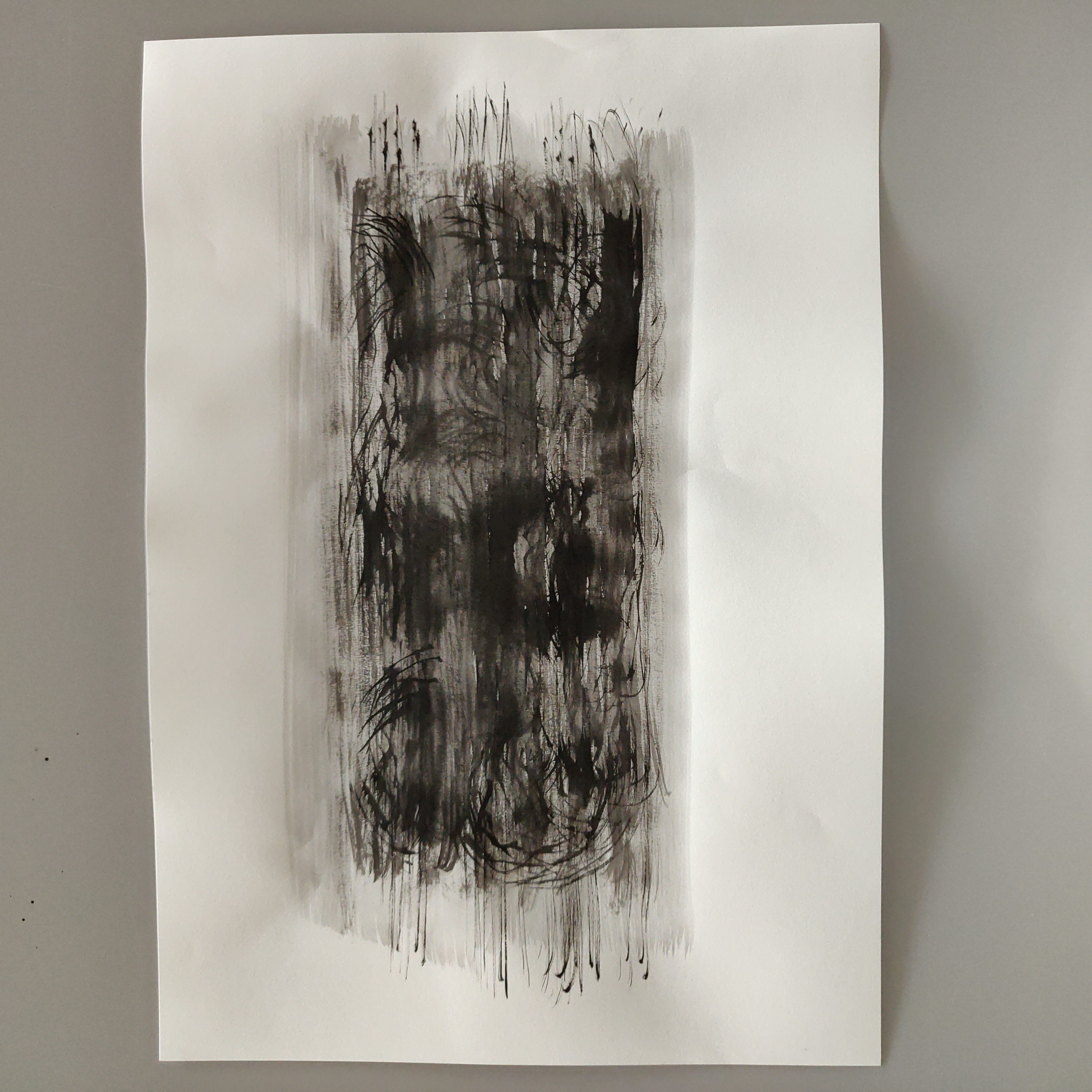 photograph of an abstract drawing, black ink on paper, light areas of grey surrounding a darker central area that runs from grey to black, swirls of ink within